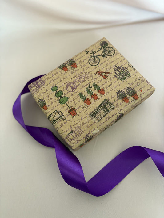 Gift box with plant-themed wrapping paper and a purple ribbon on a white background
