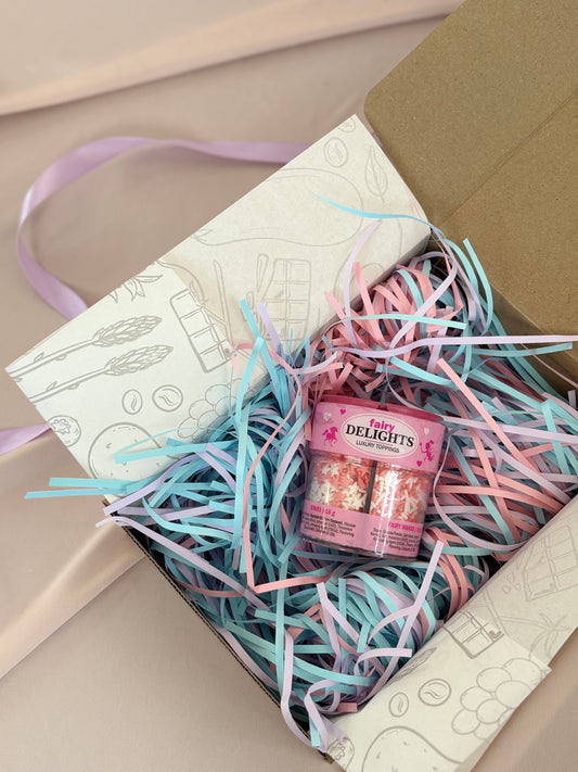 Gift box with pink and blue ribbons and a small pink container labeled 'Tulips Delights' on a beige surface.