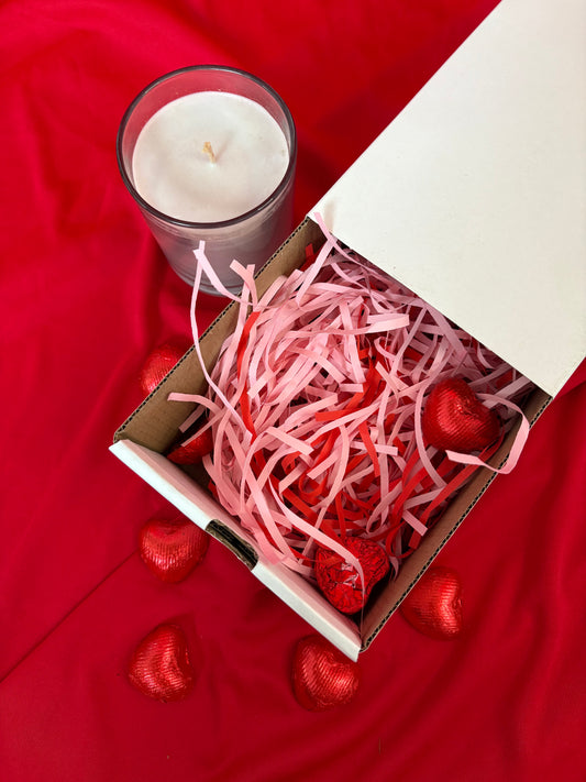 Box with pink shredded paper and red heart-shaped objects on a red fabric background