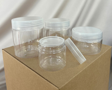Clear plastic jars with lids on a cardboard box against a neutral background