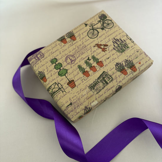 Gift box with plant-themed wrapping paper and a purple ribbon on a white background