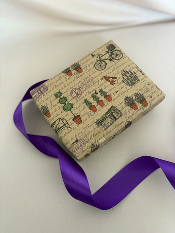 Gift box with plant-themed wrapping paper and a purple ribbon on a white background