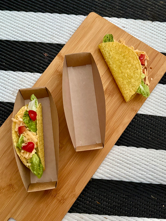 Two filled tacos on a wooden board with a striped background