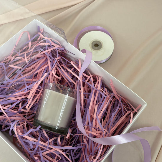 Nail polish bottle in a box with pink and purple shredded paper and ribbons.