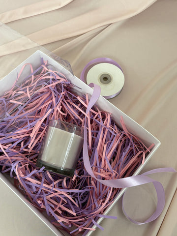 Nail polish bottle in a box with pink and purple shredded paper and ribbons.