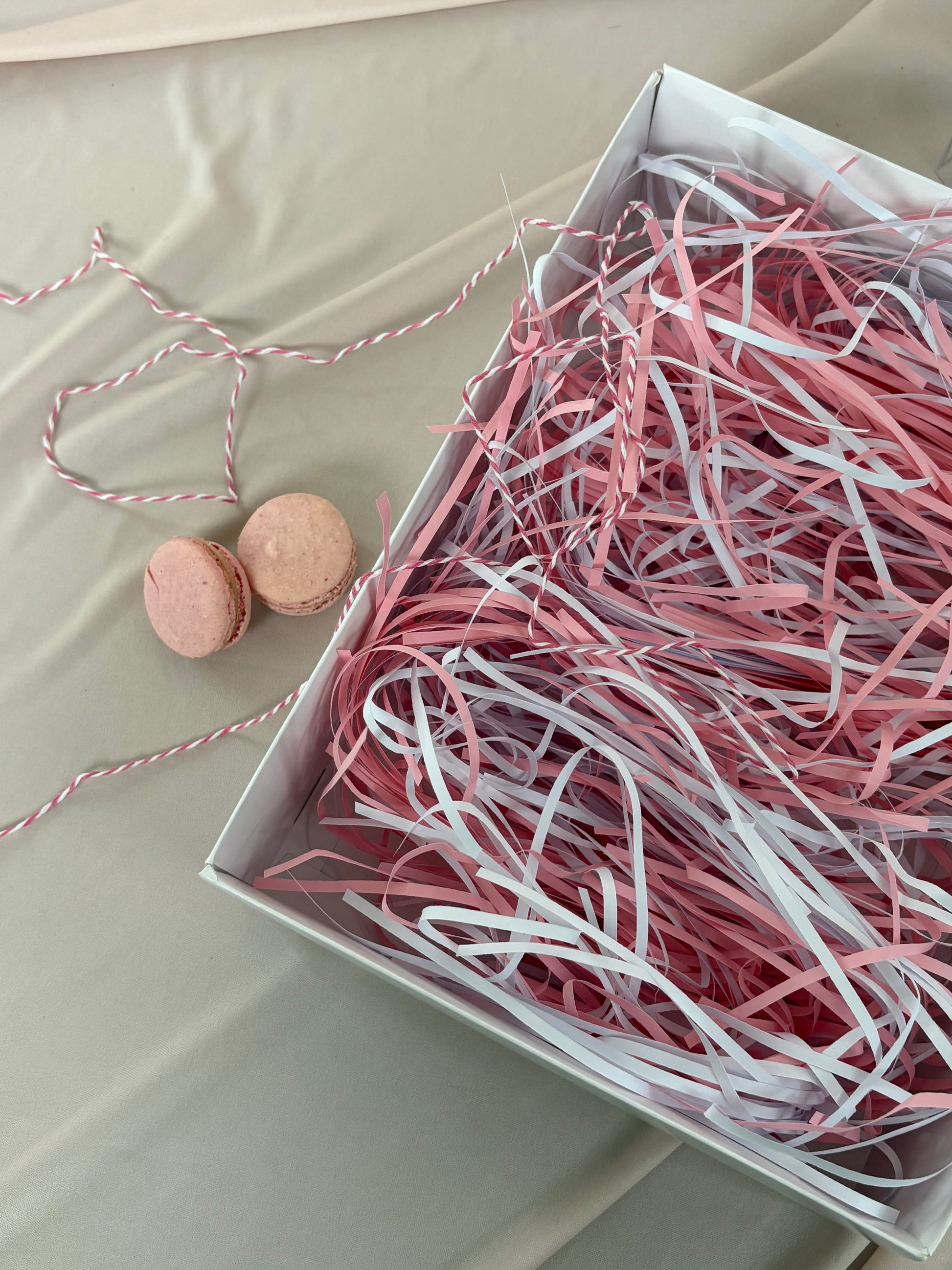 Box of pink and white shredded paper with two macarons on a light background