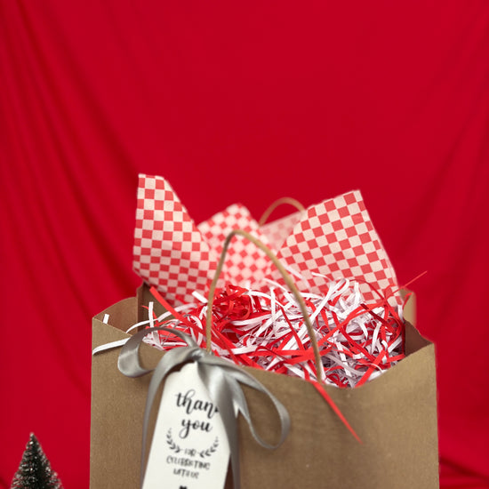 Gift bag with red and white checkered paper, red and white shredded paper, and a 'thank you' tag on a red background.