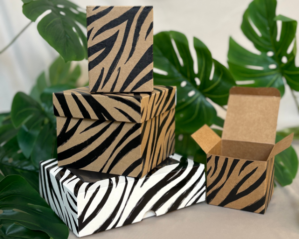 Stack of decorative boxes with zebra print design against a green leafy background