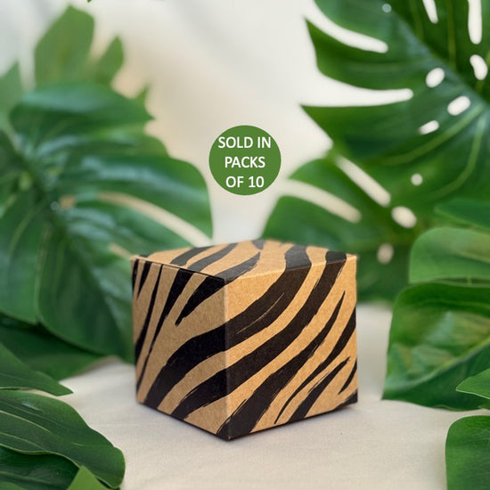 Wooden cube with zebra pattern on a white surface with green leaves in the background
