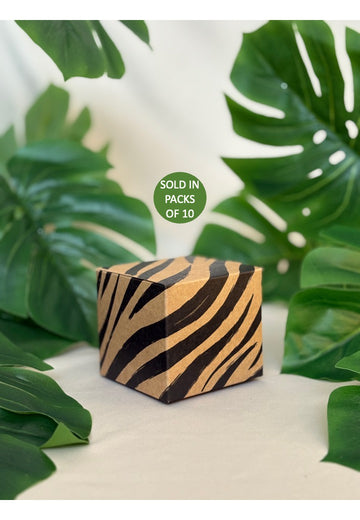 Wooden cube with zebra pattern on a white surface with green leaves in the background